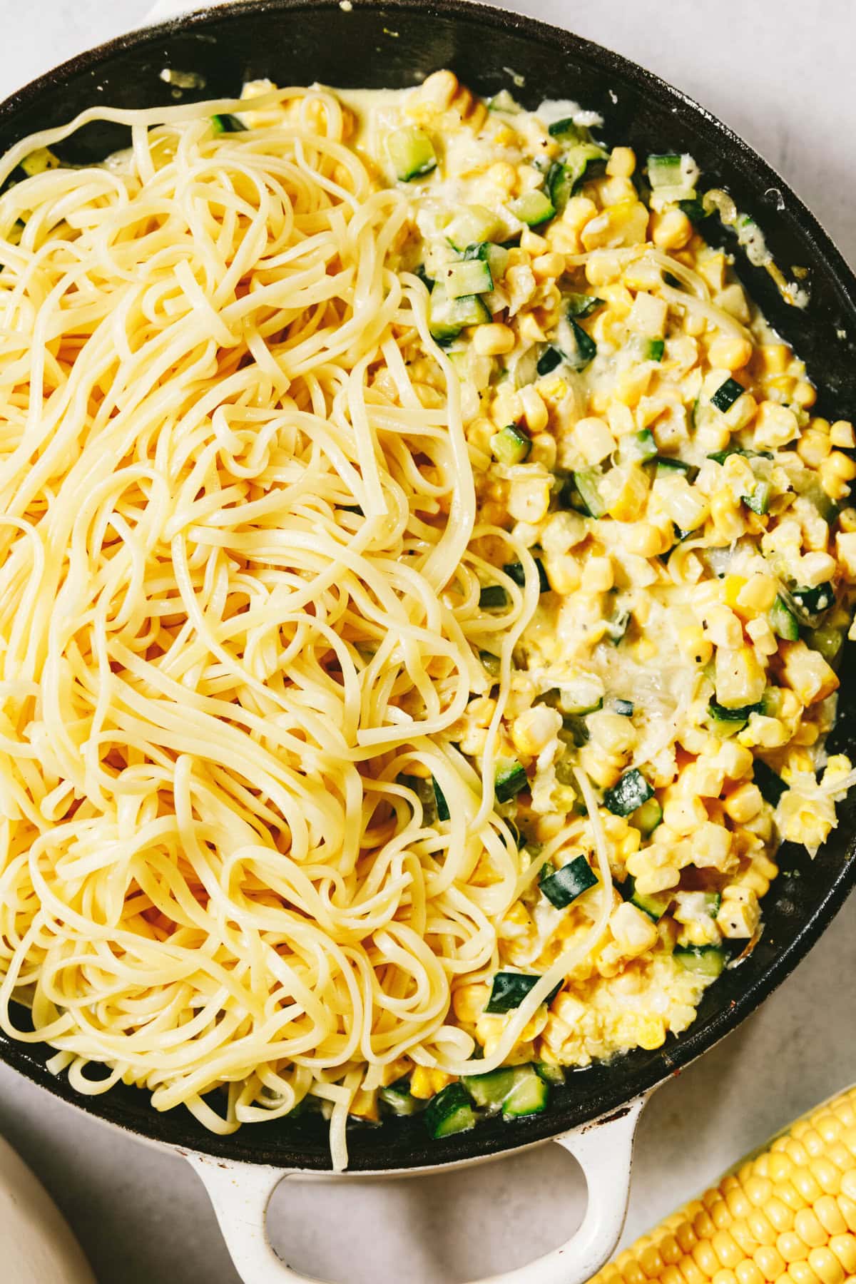 A skillet with cooked spaghetti on one side and a vibrant mix of corn, zucchini, and creamy sauce on the other creates a delightful summer squash pasta feast.