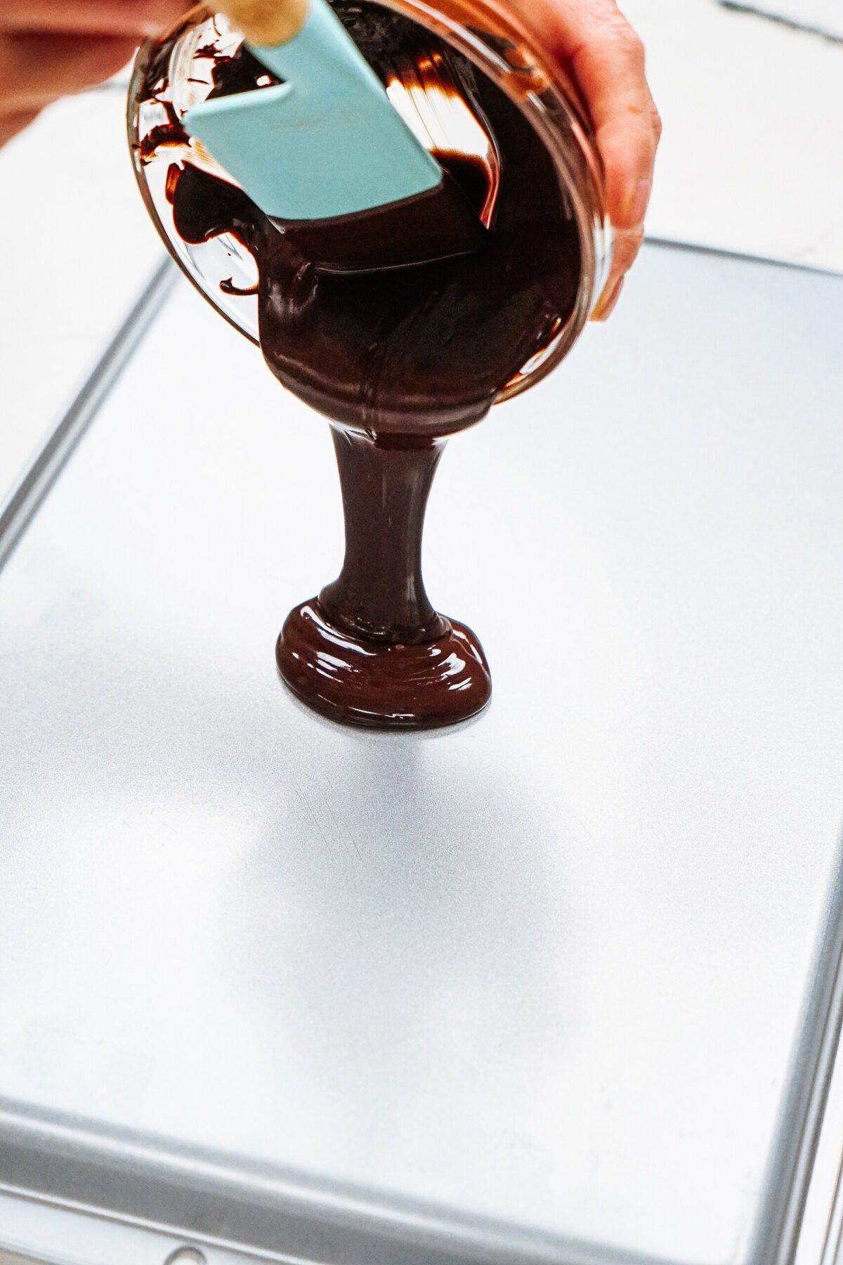 Chocolate being poured from a bowl onto a baking tray with a spatula, ready to transform into decadent chocolate curls for cake.