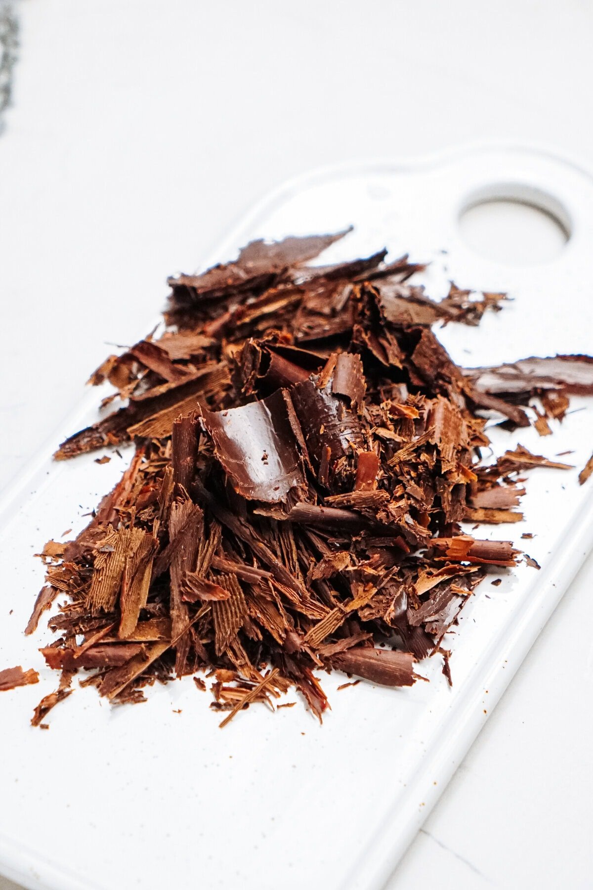 A pile of chocolate curls for cake rests gracefully on a white cutting board.