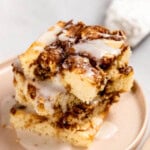 A slice of cinnamon roll cake on a plate, topped with white icing.