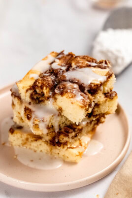 A slice of cinnamon roll cake on a plate, topped with white icing.