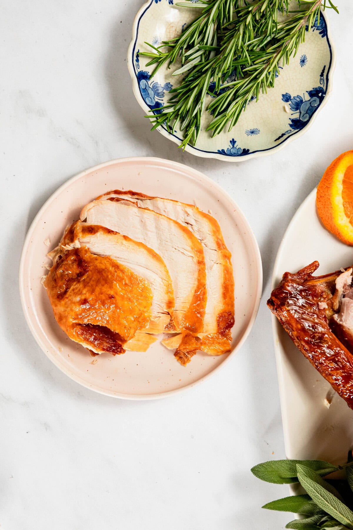 Slices of roasted turkey on a plate, with sprigs of rosemary on a floral-patterned dish nearby.