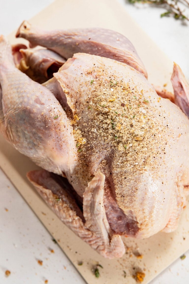 A dry brine turkey seasoned with spices and herbs sits on a cutting board, ready to transform into a flavorful masterpiece.