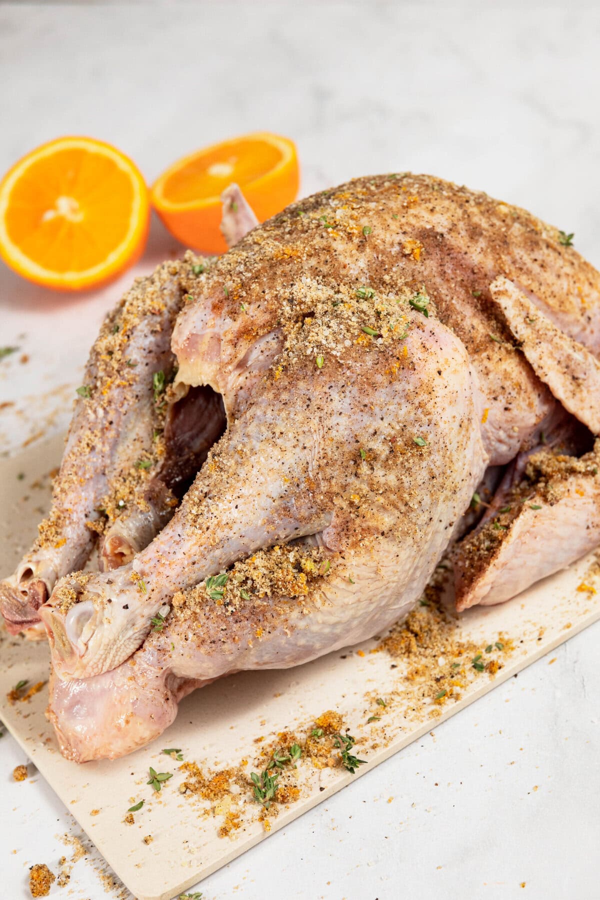 A whole turkey, seasoned to perfection with a dry brine of herbs and spices, sits invitingly on a cutting board, while two orange halves linger in the background.