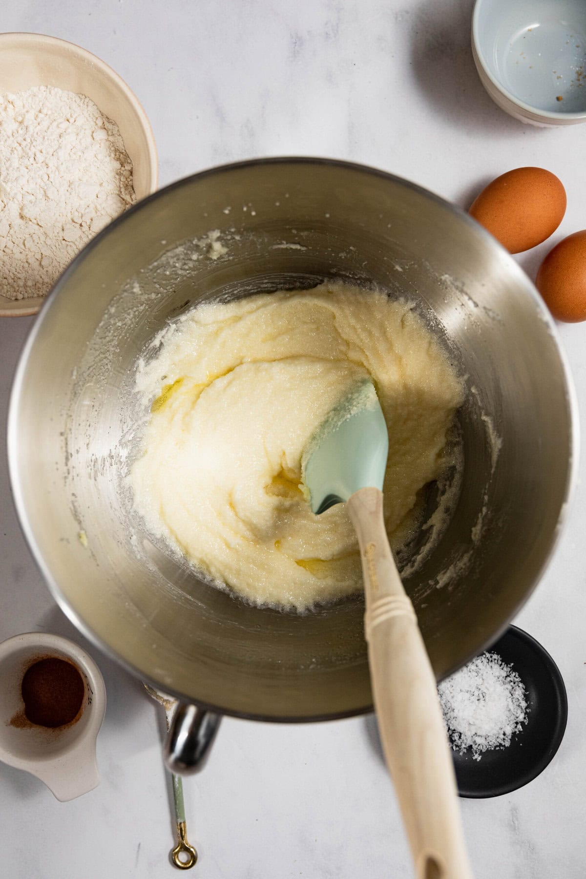 A mixing bowl with creamed butter and sugar, surrounded by flour, eggs, vanilla, and salt.