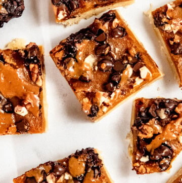 Close-up of dessert bars topped with chocolate chips, nuts, and caramel on a white background.