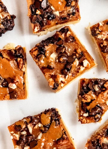 Close-up of dessert bars topped with chocolate chips, nuts, and caramel on a white background.