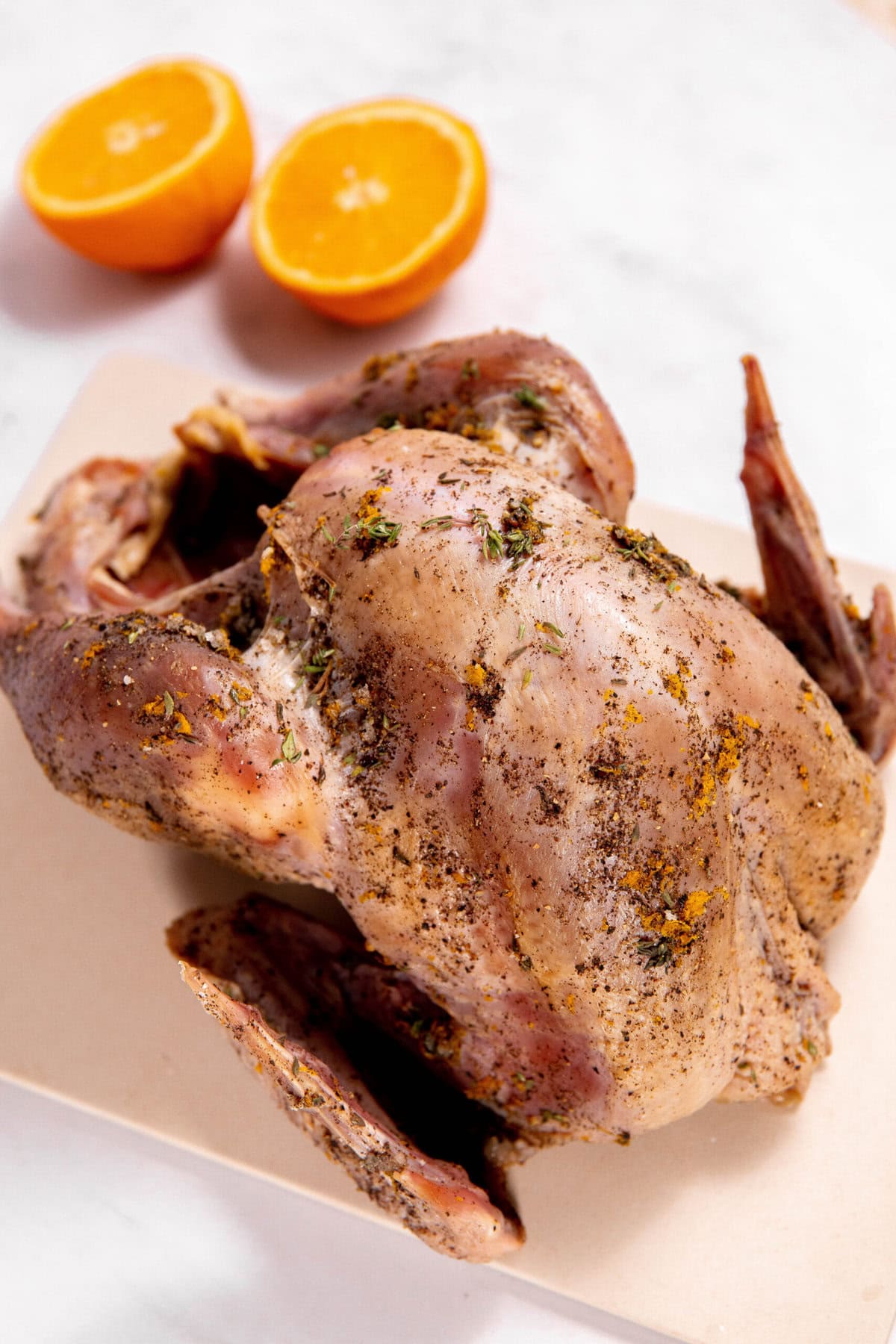 Dry brine turkey rests on a cutting board, its seasoned exterior promising rich flavors. In the background, two halved oranges add a touch of citrus zest waiting to enhance the savory delight.