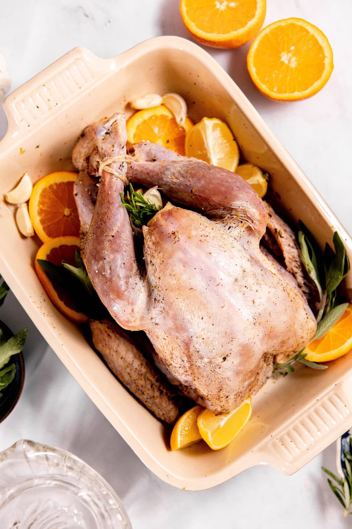 Dry brine turkey nestled in a baking dish with orange slices, garlic cloves, and herbs creates a flavorful feast ready for the oven.