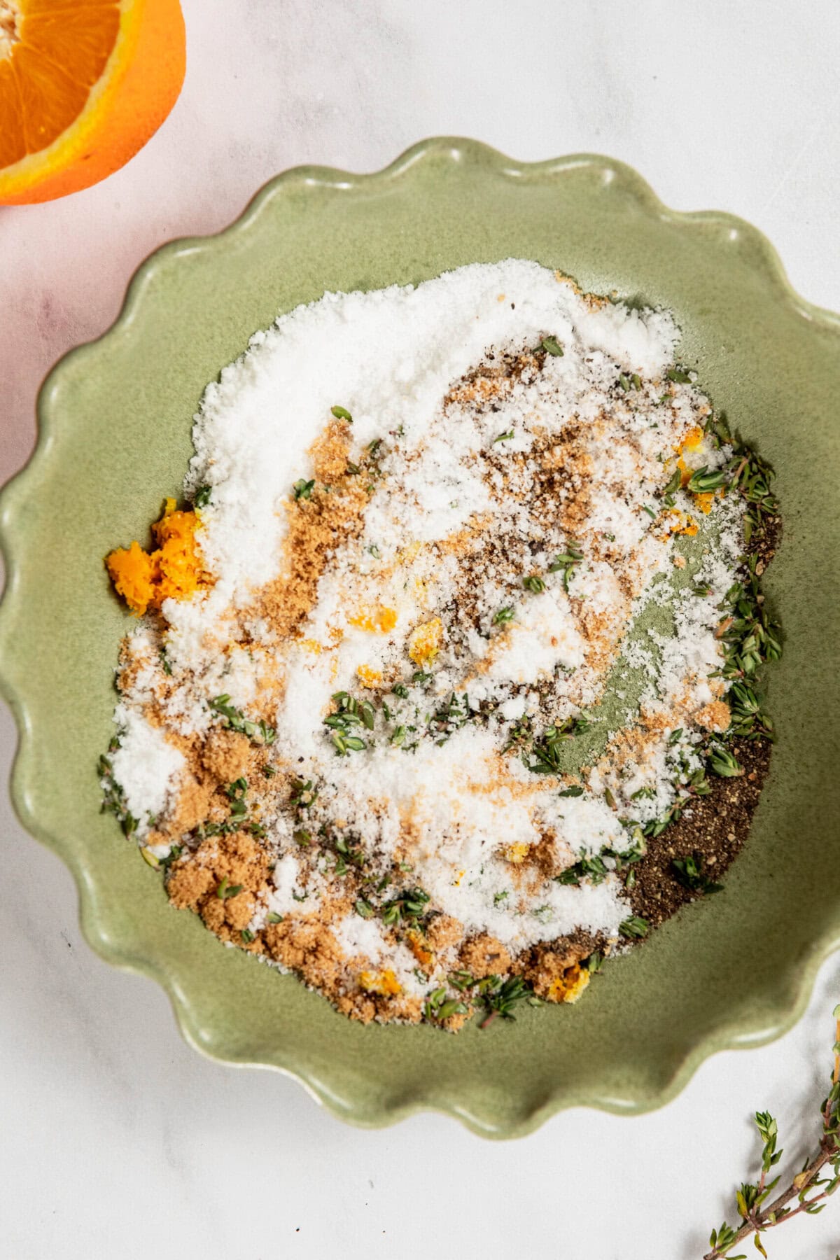 A green bowl, perfectly paired with dry brine turkey, holds a mixture of sugar, brown sugar, herbs, and orange zest on a white surface.