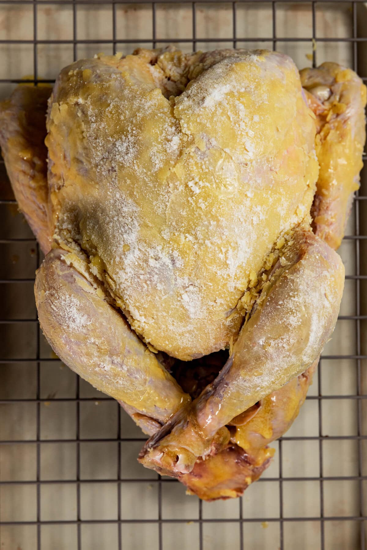 Uncooked, flour-dusted chicken on a wire rack.