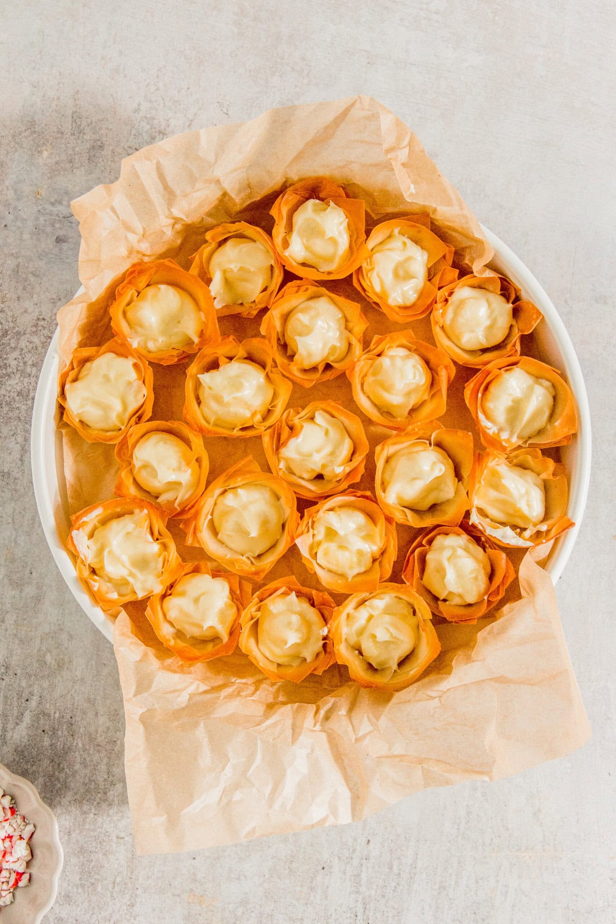 A plate of phyllo cups filled with creamy filling, arranged in a circular shape on parchment paper.