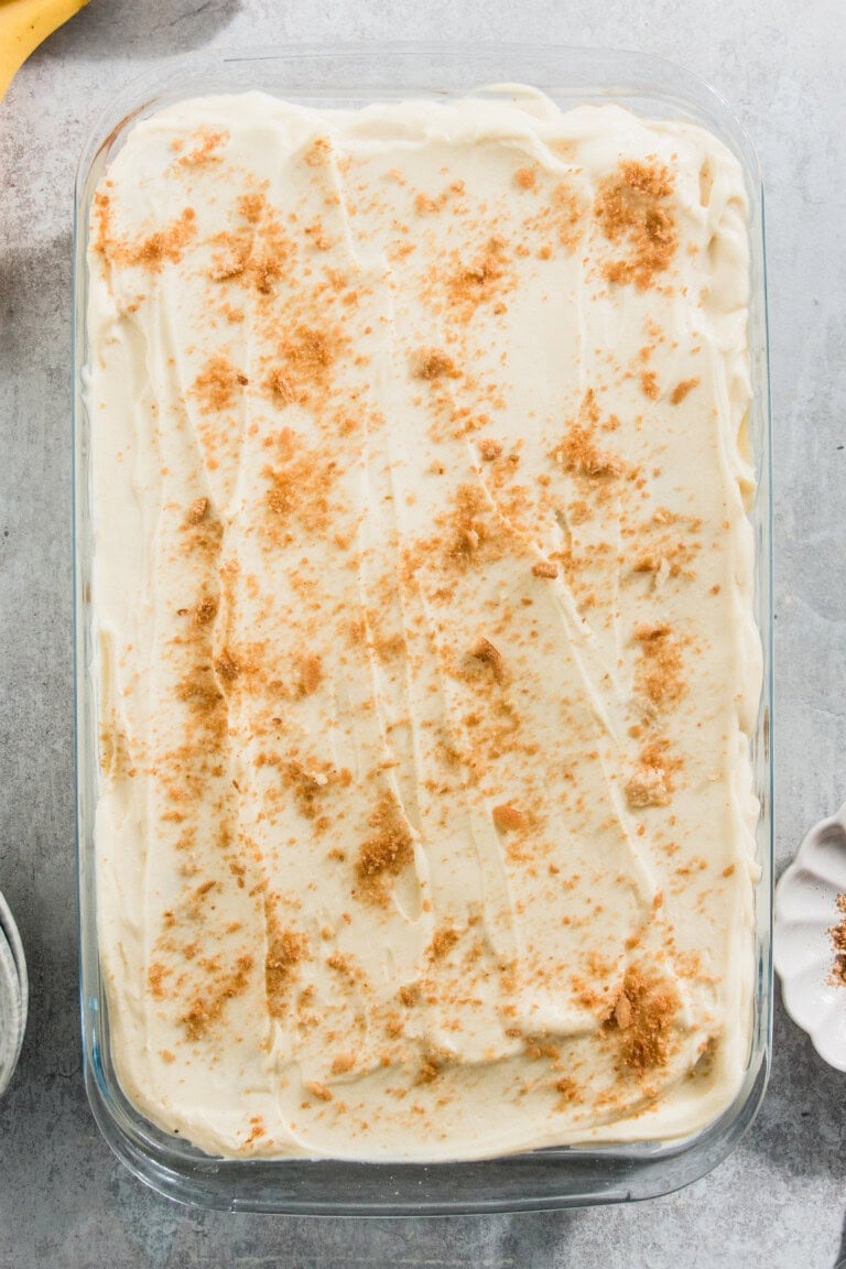 A rectangular dish of banana pudding topped with brown sugar crumbles sits on a grey surface.