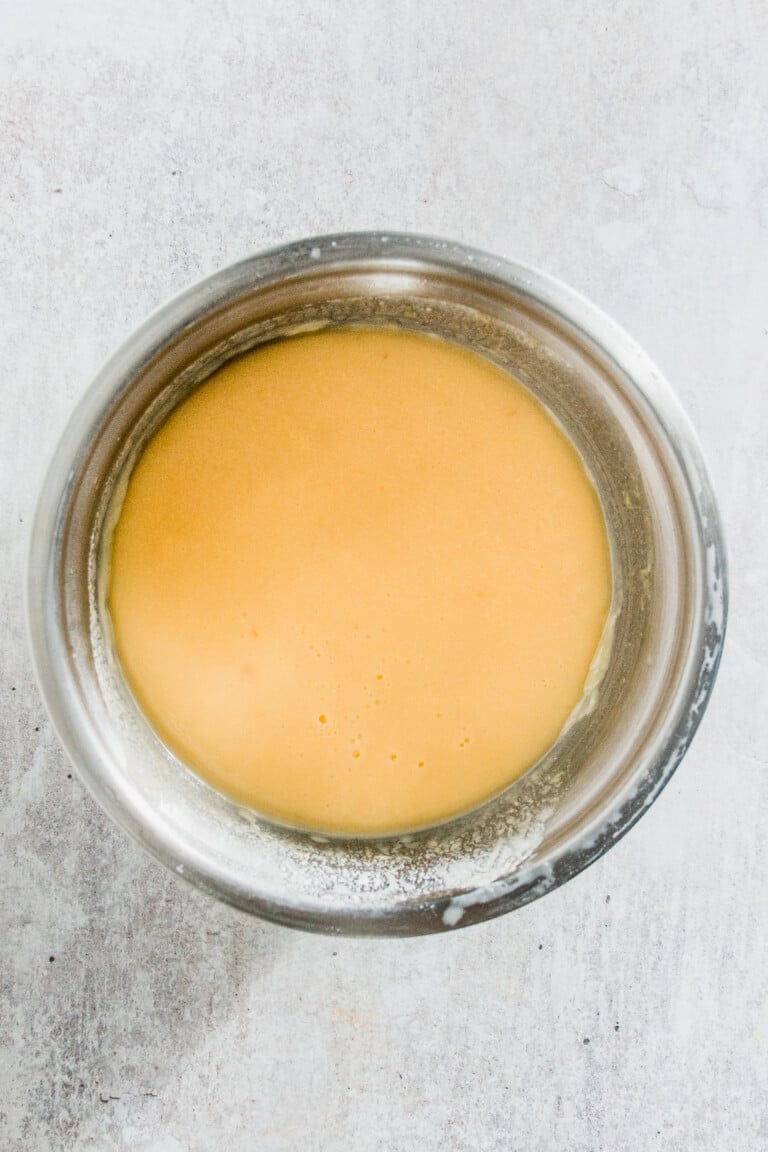 A stainless steel bowl filled with smooth, light orange batter sits on a gray surface.