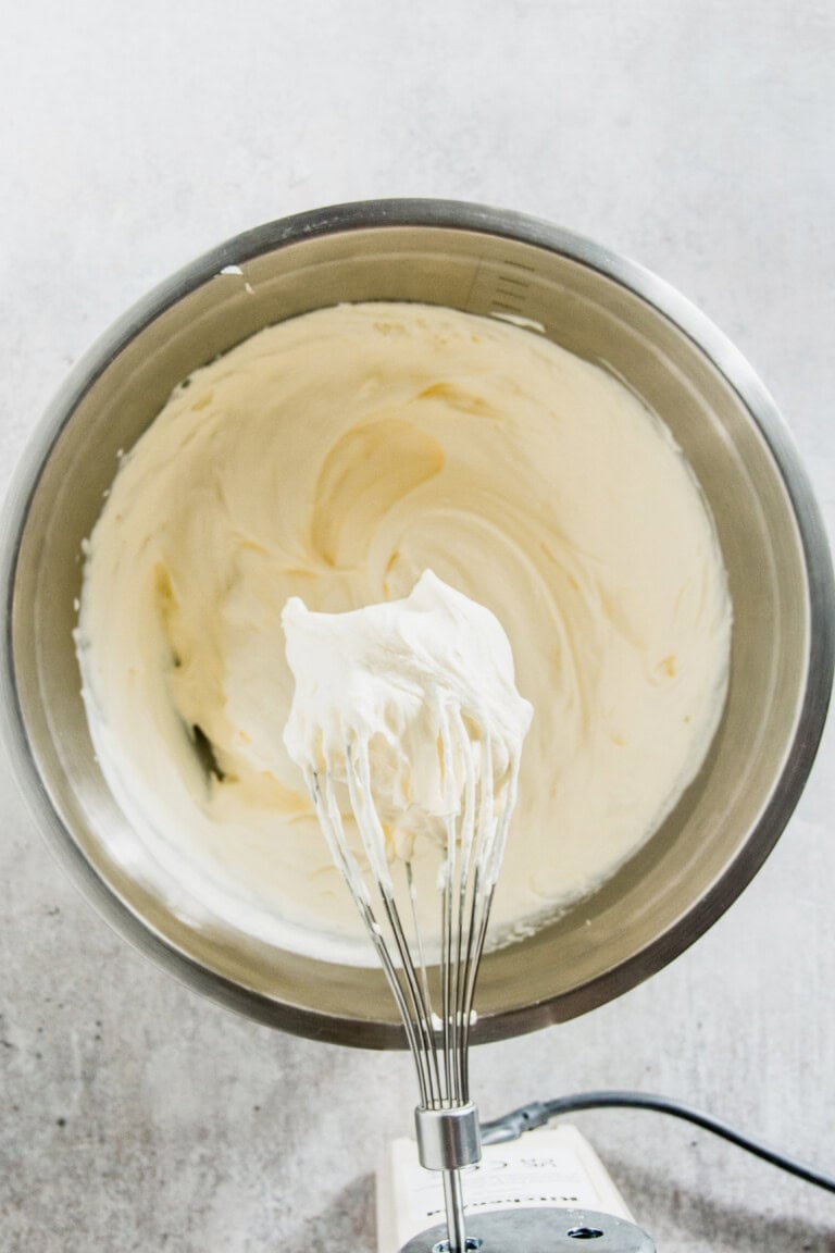 A whisk with smooth, creamy batter in a large metal mixing bowl.