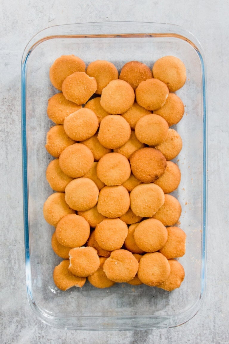 A rectangular glass dish filled with round vanilla wafer cookies arranged in rows on a light surface.