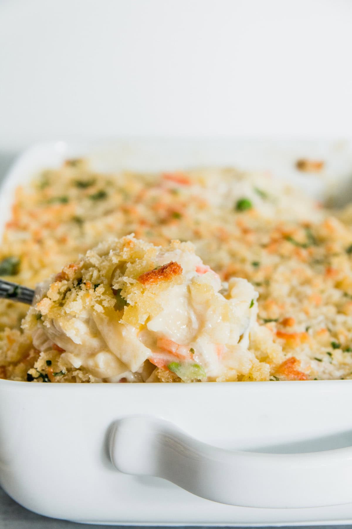 A serving of creamy chicken casserole with breadcrumbs being lifted from a white baking dish.