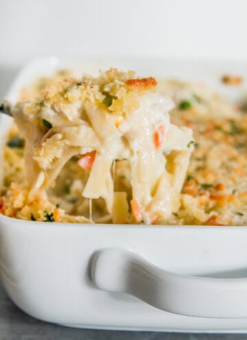 A close-up of a serving of creamy chicken casserole pasta with a golden breadcrumb topping in a white dish.