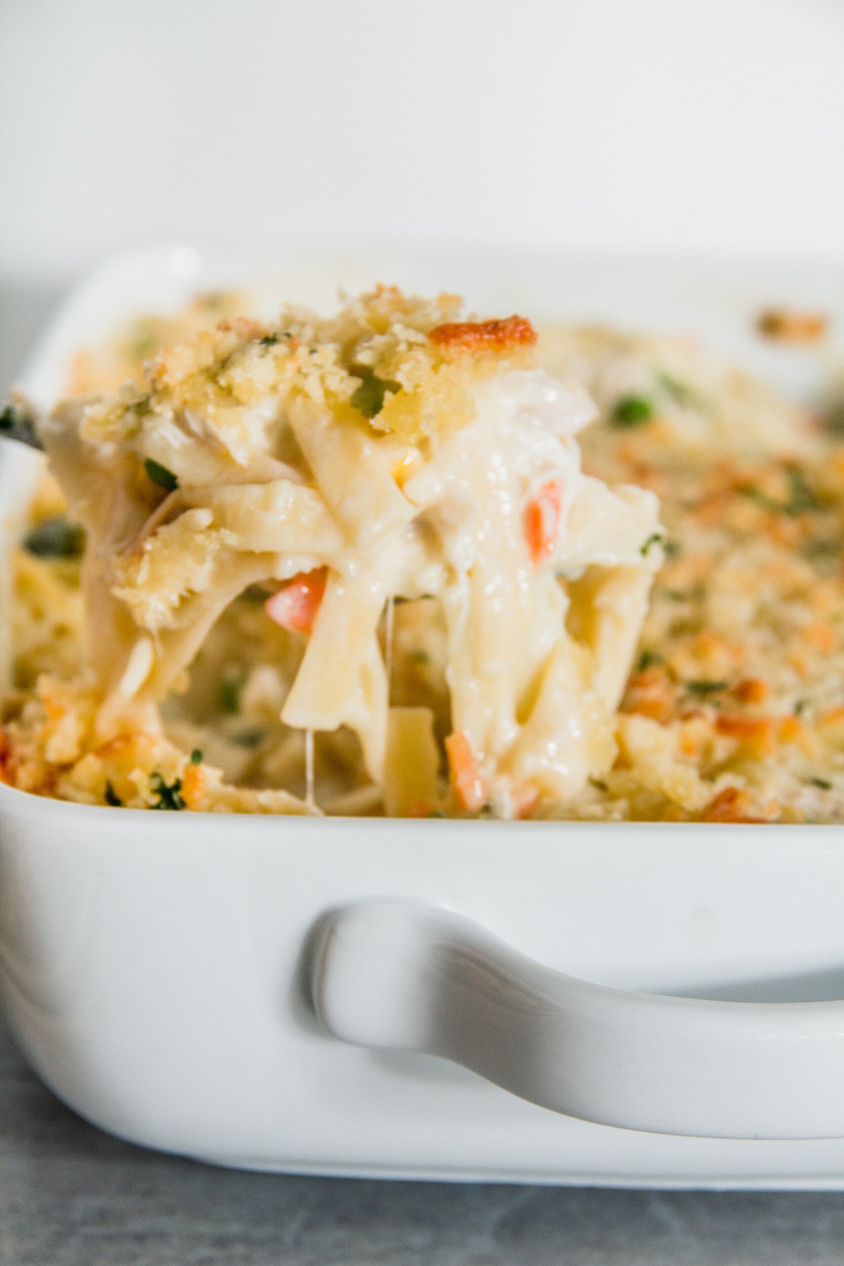 A close-up of a serving of creamy chicken casserole pasta with a golden breadcrumb topping in a white dish.