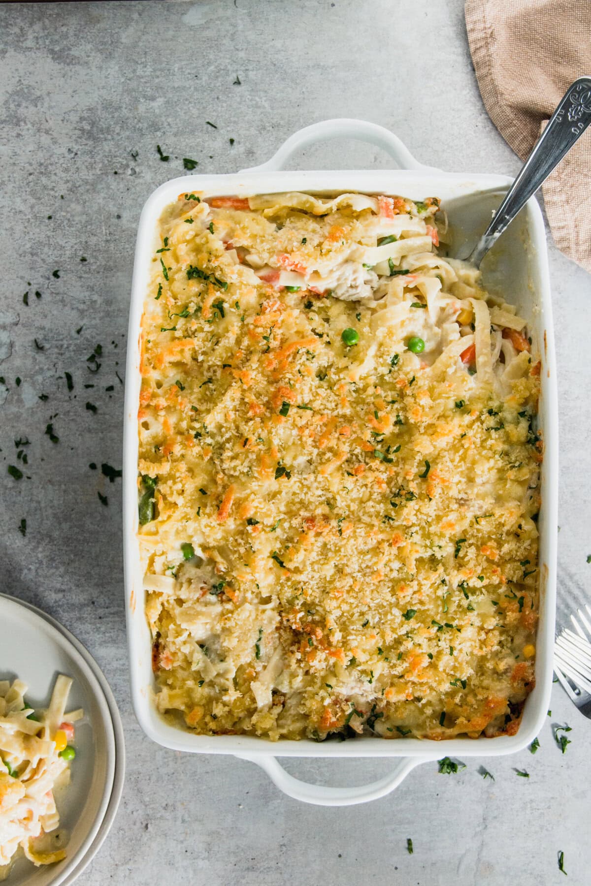 Baked chicken casserole in a rectangular dish with a crumbly topping, served on a plate next to it.