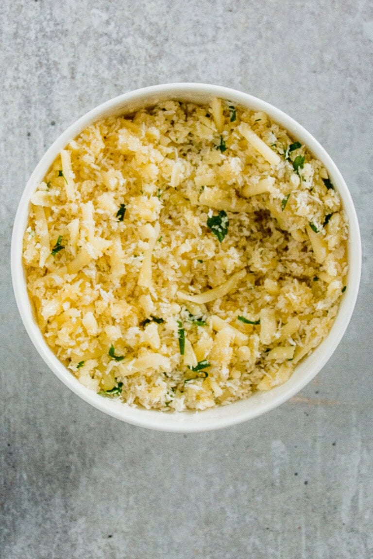 Bowl of grated cheese mixed with herbs on a gray surface.