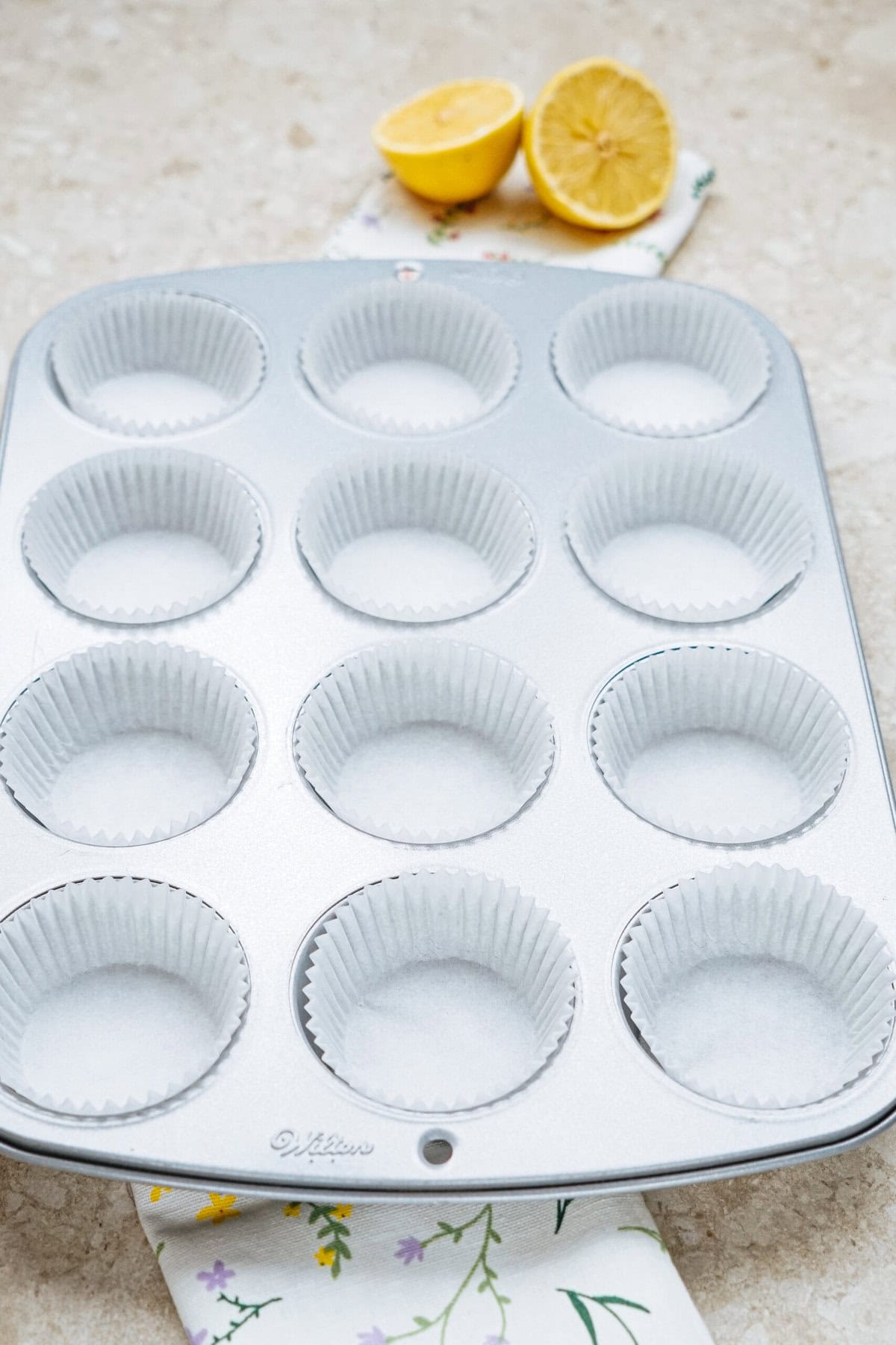 Muffin tin lined with paper cups on a countertop, with a halved lemon in the background.