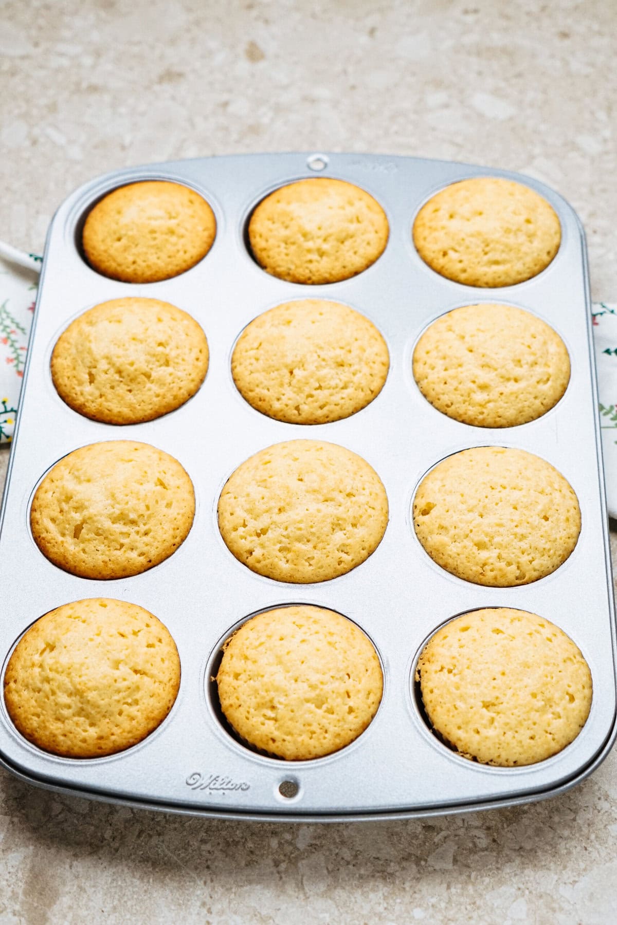 A tray of twelve freshly baked muffins in a muffin tin on a light-colored countertop.