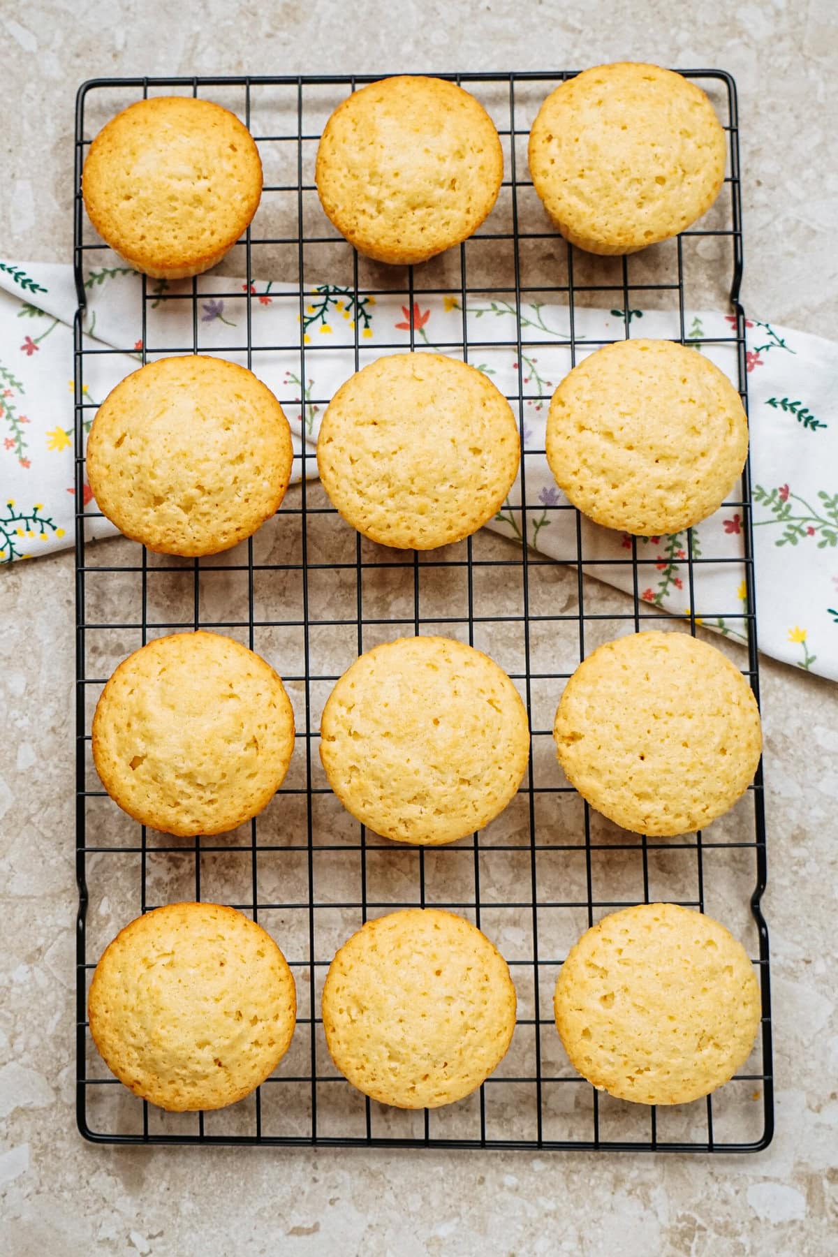 Twelve golden muffins cooling on a wire rack, set on a flower-patterned cloth background.