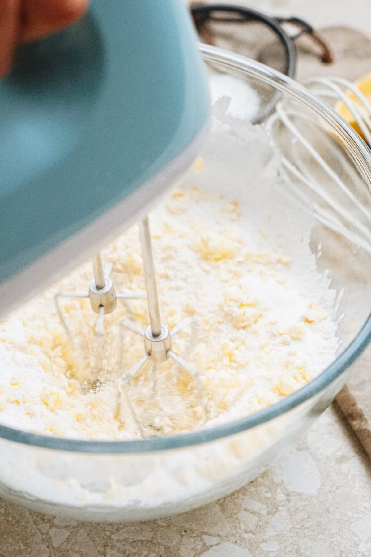 Close-up of an electric mixer blending ingredients in a clear glass bowl, creating a creamy mixture.