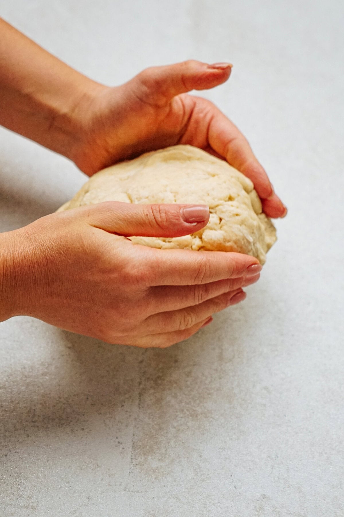 Hands shaping a ball of dough on a light surface.