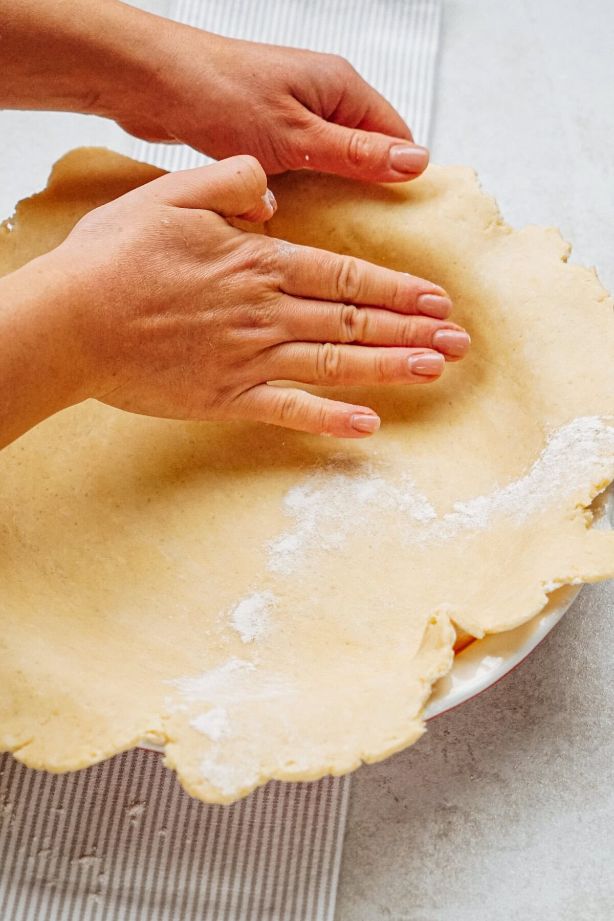 Hands pressing dough into a pie dish on a striped cloth.