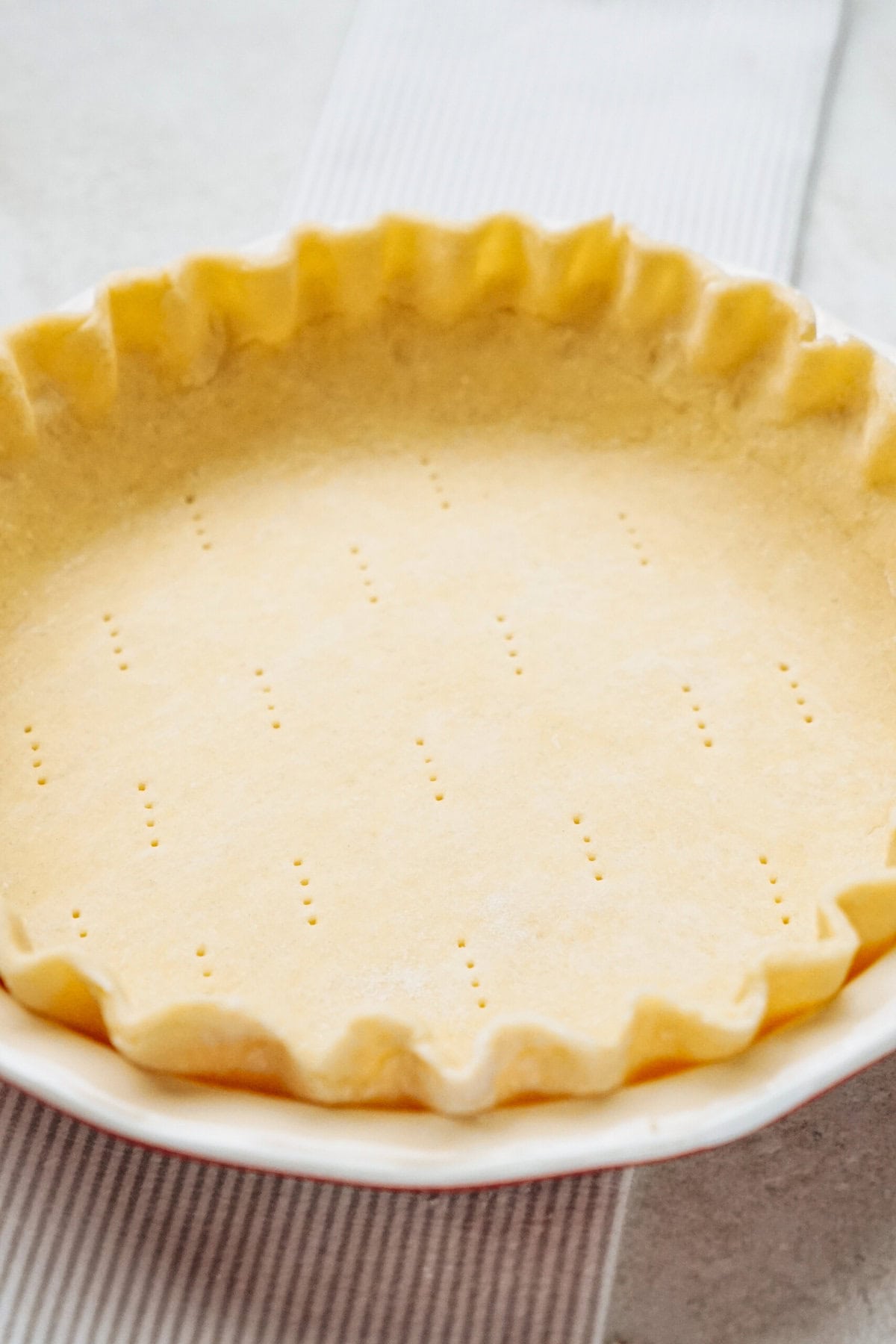 Unbaked pie crust in a fluted pie dish with fork marks on the bottom.