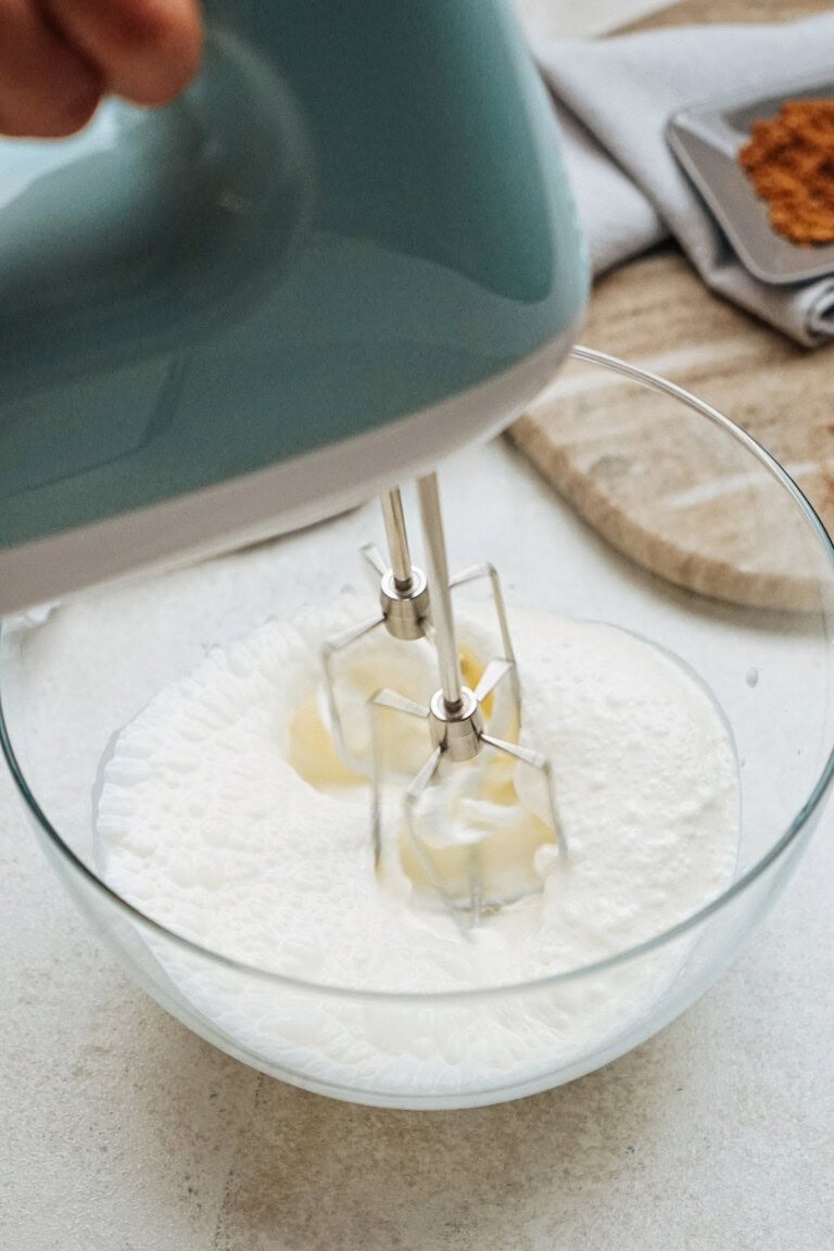 Hand mixer blending ingredients in a glass bowl on a kitchen counter.