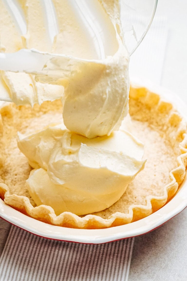 Filling a pie crust with creamy, pale yellow custard from a mixing bowl.