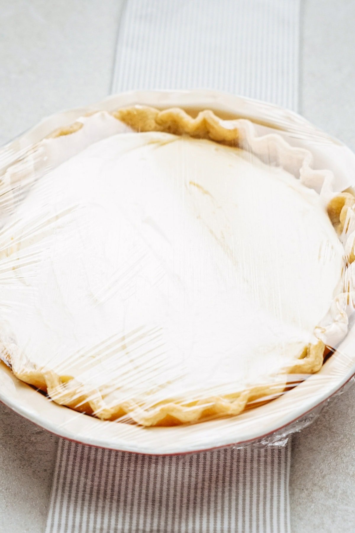 A pie covered with plastic wrap is placed on a striped cloth.