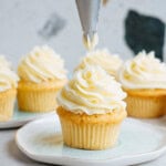 Piping frosting onto vanilla cupcakes arranged on a light blue plate.