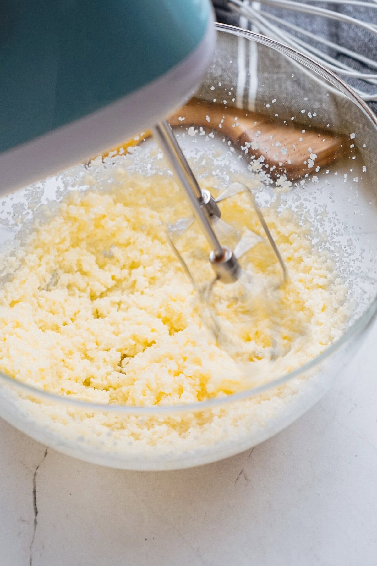 A hand mixer blends butter and sugar in a glass bowl, creating a light, fluffy mixture.