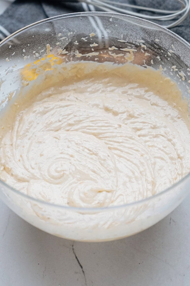 A glass bowl filled with creamy pancake or cake batter on a white surface.