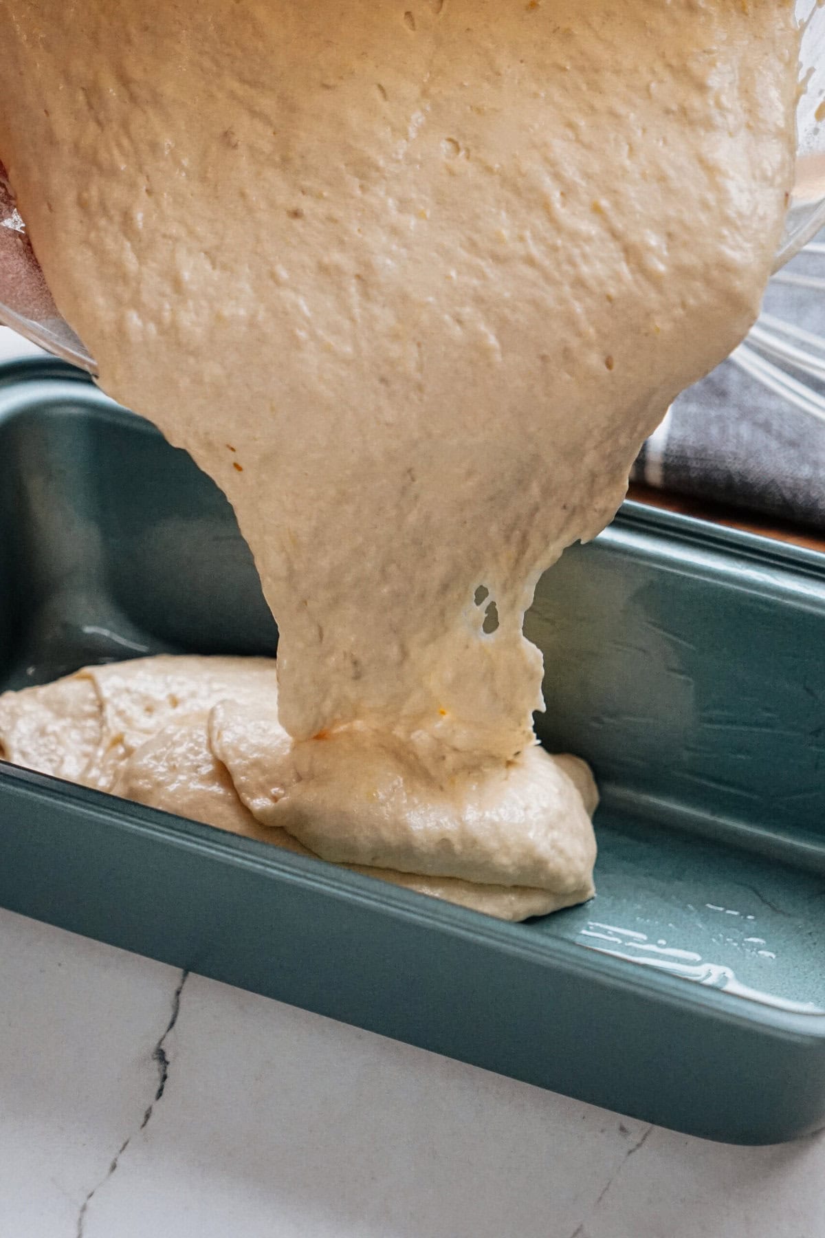 Batter is being poured into a rectangular baking dish on a marble countertop.