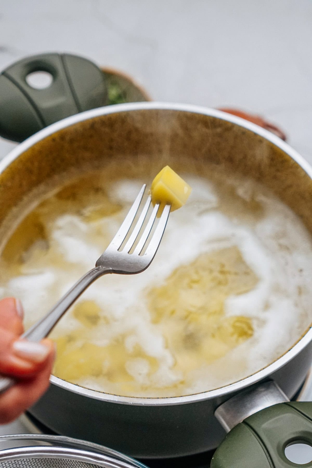 A piece of pasta is held on a fork over a steaming pot of boiling pasta.