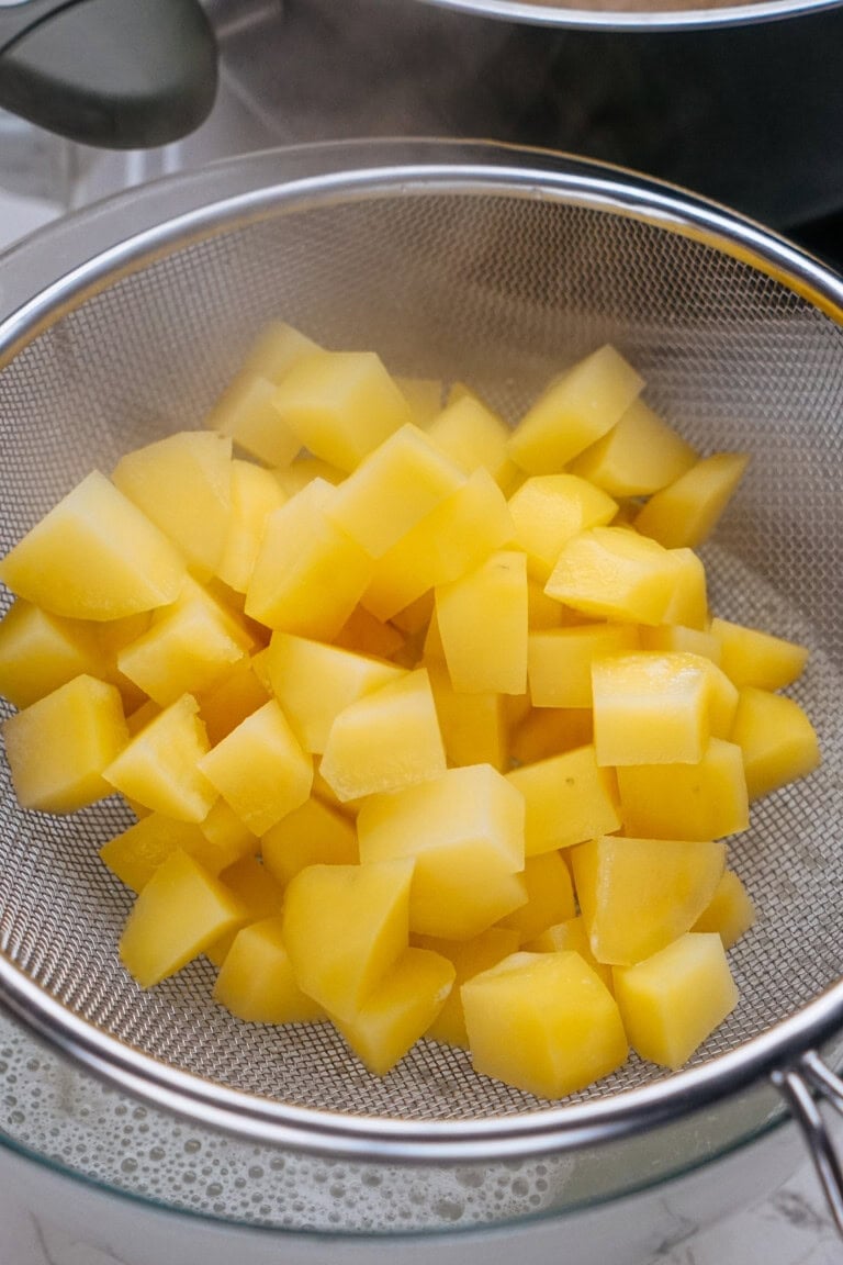 Steaming diced potatoes in a metal strainer over a bowl.