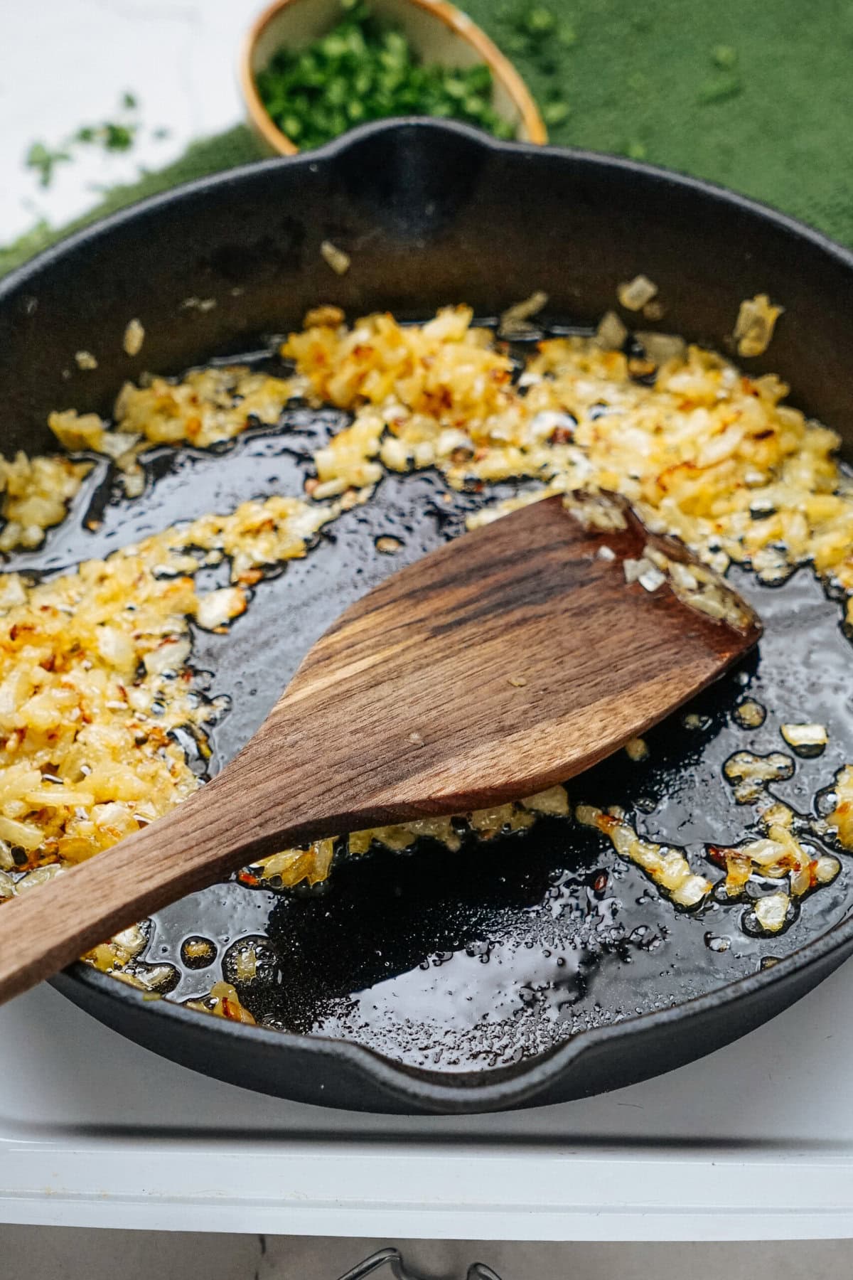 Chopped onions sautéing in oil in a cast iron skillet with a wooden spatula.