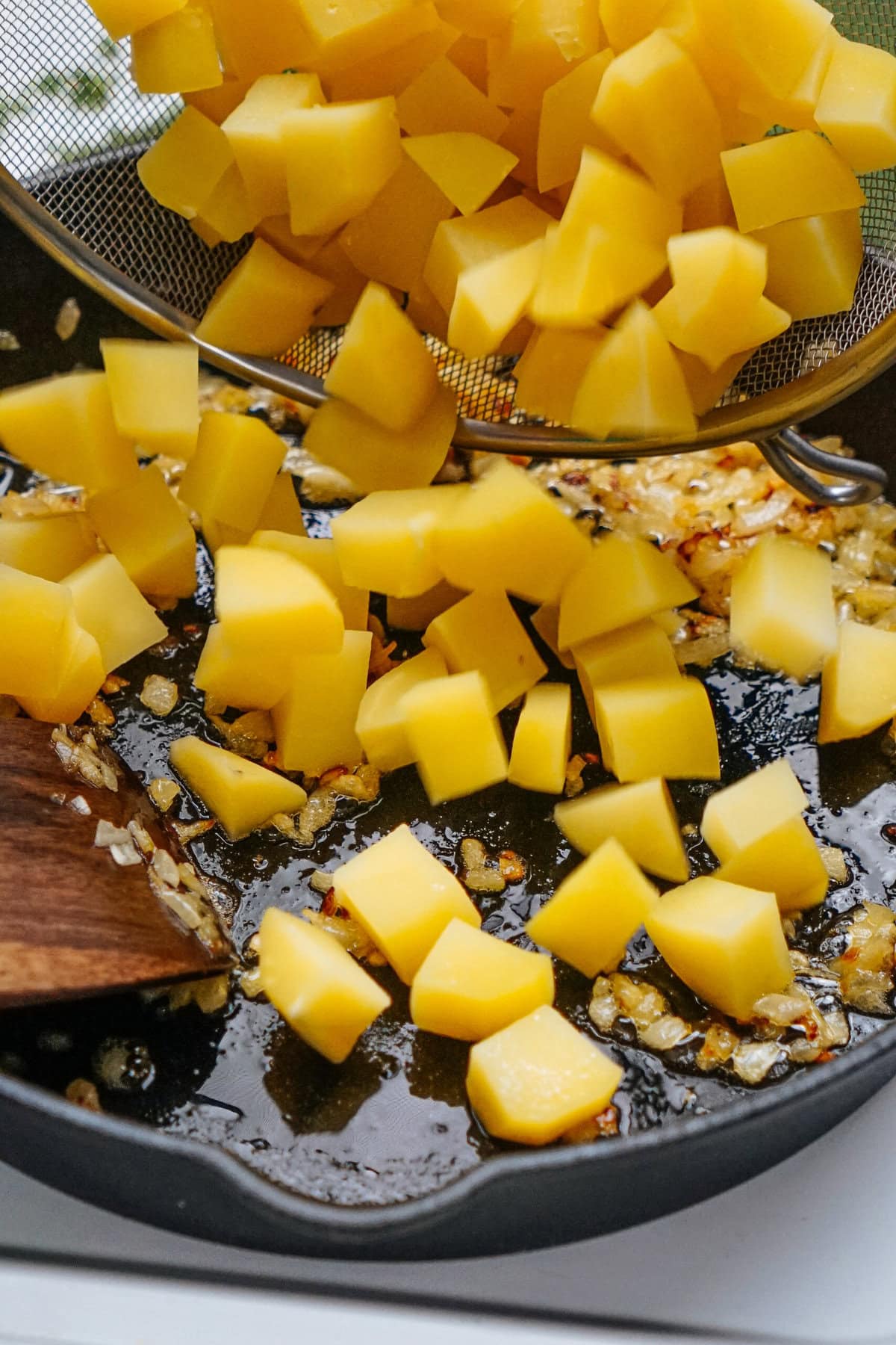 Diced yellow potatoes being added to a pan with sautéed onions.