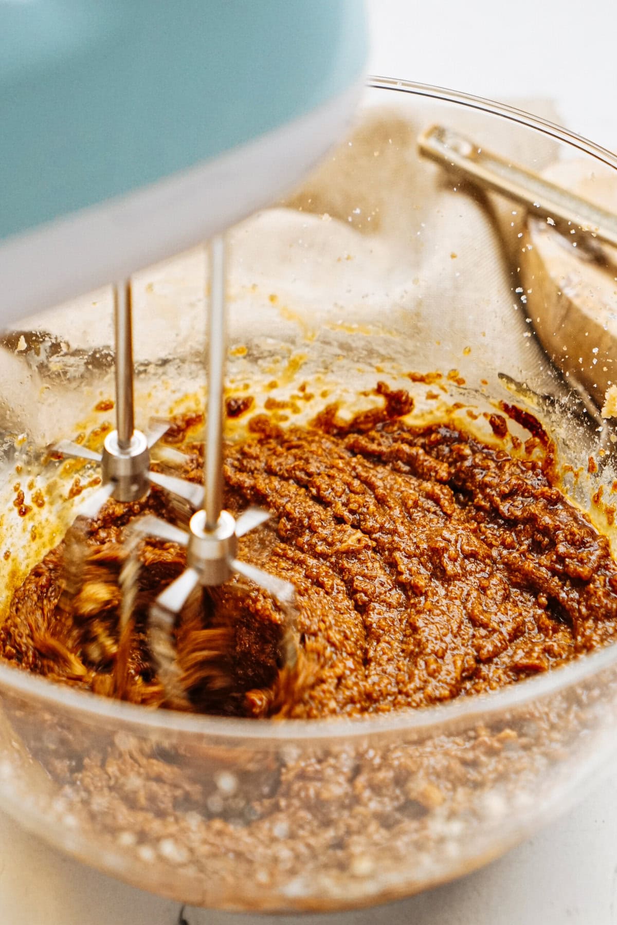 A hand mixer blends a delicious ginger cookie mixture in a glass bowl, with visible motion blur from the mixer blades.