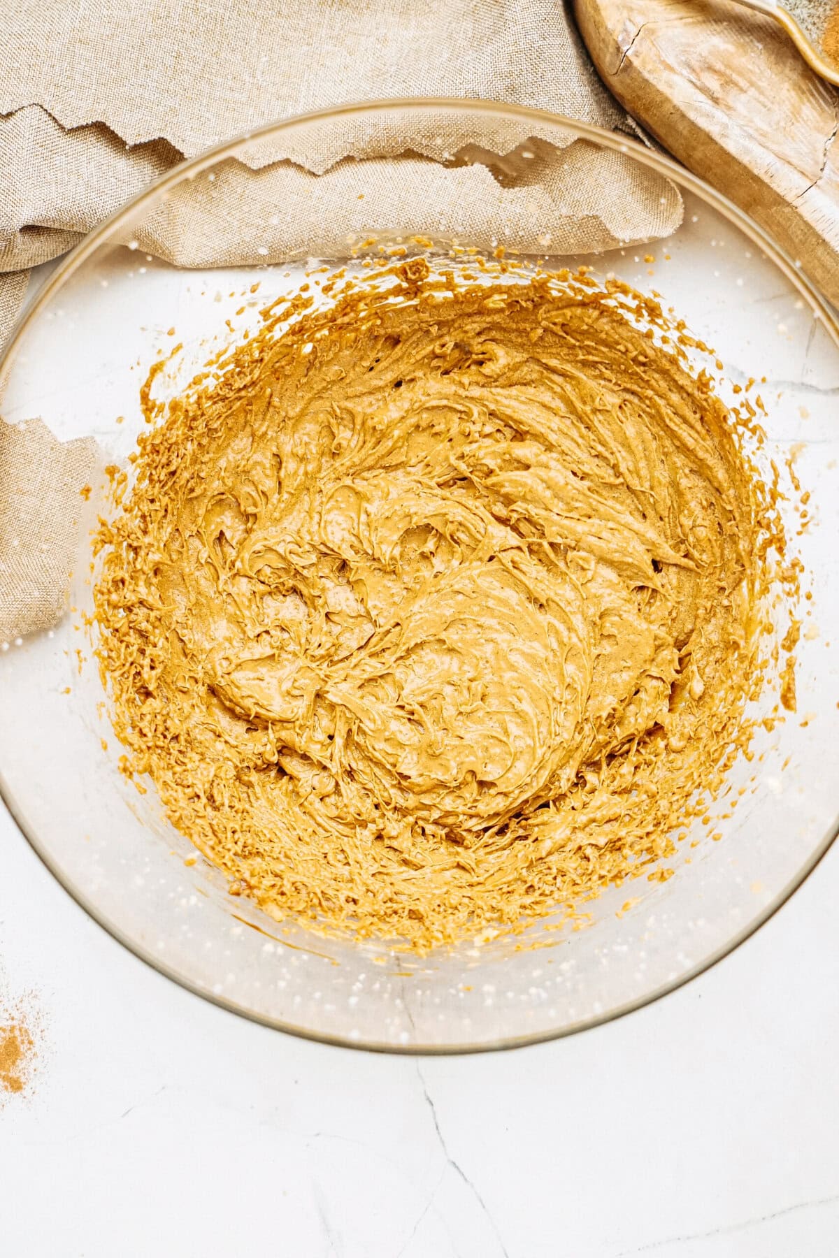 A glass bowl filled with smooth peanut butter batter, perfect for making ginger cookies, rests on a beige cloth.