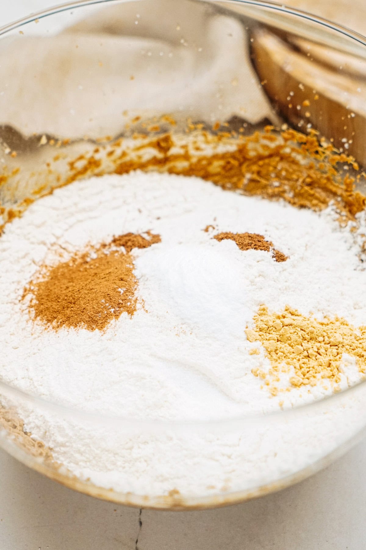 A glass bowl containing flour, baking soda, and spices, including cinnamon and ginger, is displayed on a countertop, ready to transform into delicious ginger cookies.