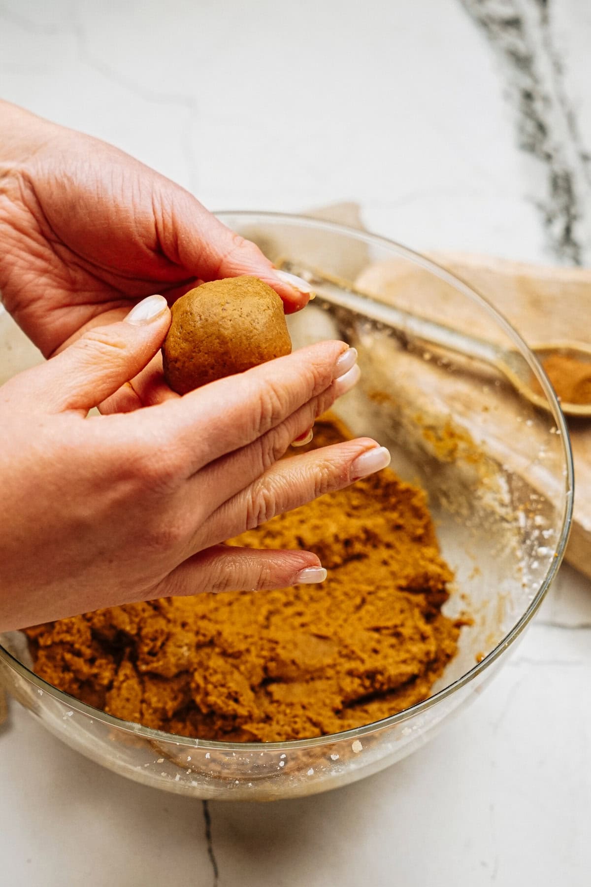 Hands rolling dough into a ball over a glass bowl with brown dough on a kitchen counter.