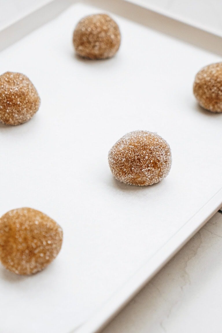 Five sugar-coated cookie dough balls on a white baking tray.