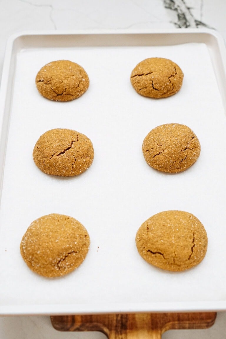 Six round ginger cookies on a baking sheet lined with parchment paper.