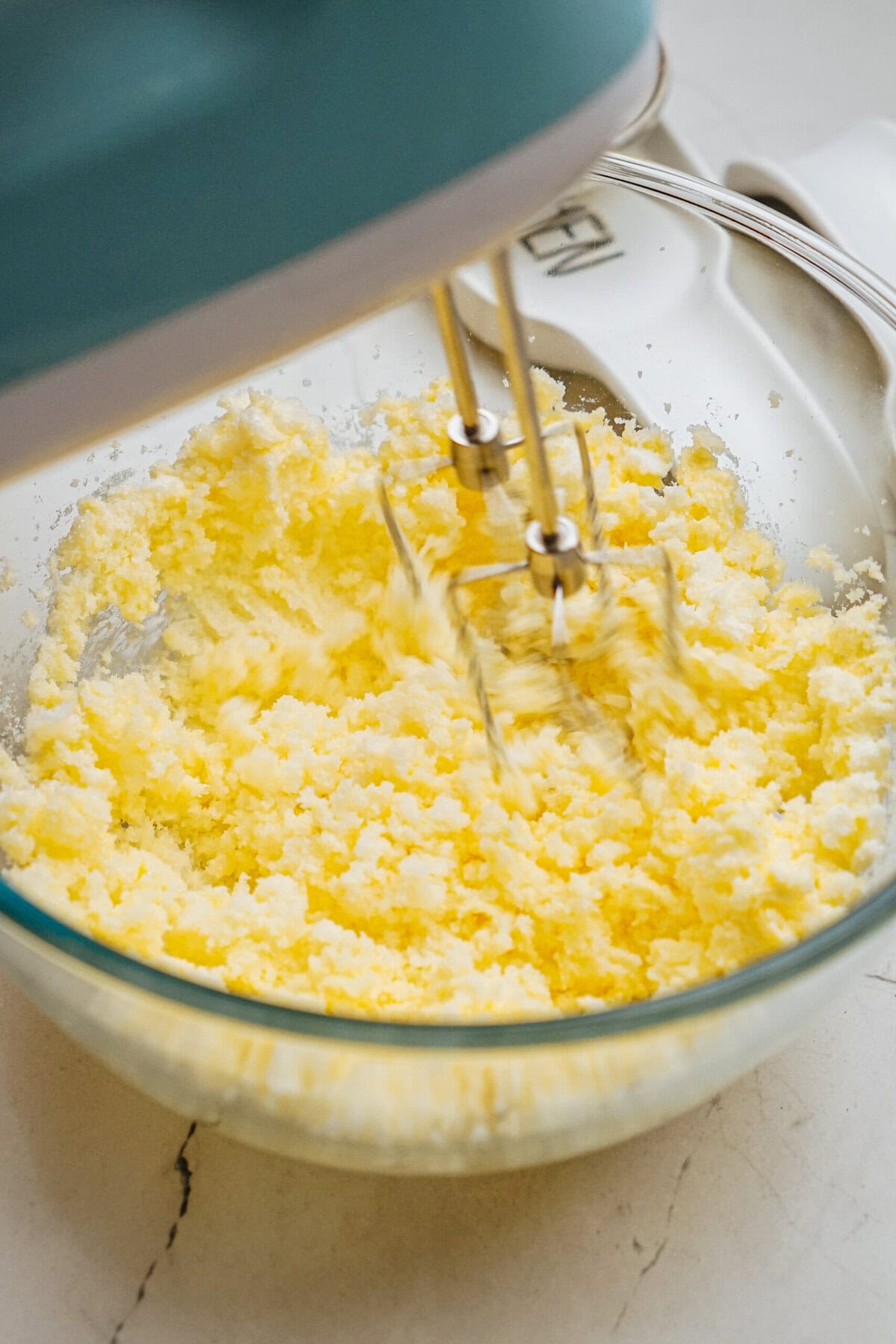 An electric hand mixer blending butter and sugar in a glass bowl on a kitchen countertop.